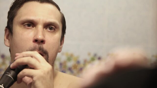 a man shaves his stubble. the guy cleans his beard with an electric razor. morning treatments in the bathroom. half of the beard close-up. copy space