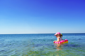 Little girl in bikini swimming in sea with swimming circle