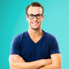 Portrait image of handsome happy man wearing in glasses, casual smart clothing, with crossed hands. Aqua marine blue color background, square composition. Caucasian male model in eyewears at studio.