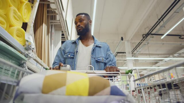 Low angle view of african man shopping in diy store putting materials from shelf in cart