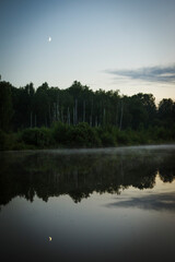 Fototapeta na wymiar reflection of clouds, moon and forest in the lake with fog