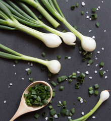 Pile of green onion and herb chopped in wooden spoon. Stone background. Top view.