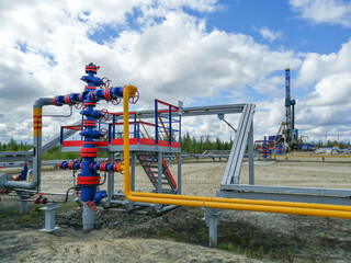 Pipeline manifold of gas wells of producing gas wells in the northern field. High pressure gate valve handwheels, pipelines. In the background, a drilling rig. Blurring distant objects.