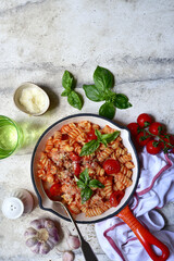 Fusilli pasta with tomatoes and garlic in a skillet. Top view with copy space.