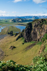 Iceland "Golden circle" journey. Top view from the cliff. Spring landscape - green volcanic meadows, the spread river, clear blue sky with fleece clouds and mountains with snowy peaks in Iceland.