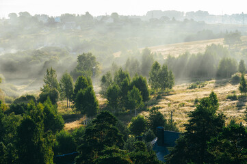 Airscape - The morning mist is hovering over the small town among thick forest. Sun's rays break beautifully through the haze. The birds-view of a town with deep forest and dollhouses