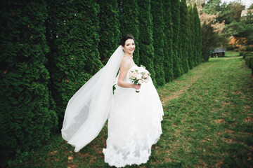 Beautiful bride in elegant white dress holding bouquet posing in park