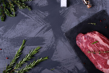 Raw marbled beef steak, herbs and spices against the grey background. Copy space
