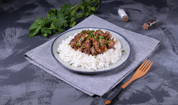 Stewed chicken gizzards on the boiled rice. Hot meal with offal meat products