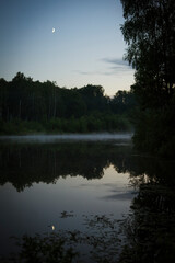 Fototapeta na wymiar sunset over the lake in forest with fog, reflection of trees in the lake