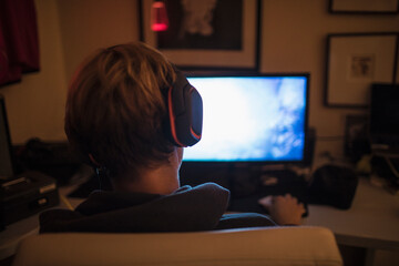 Teenage boy with headphones playing video game in dark bedroom