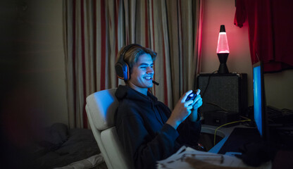 Smiling teenage boy playing video game at computer in dark bedroom