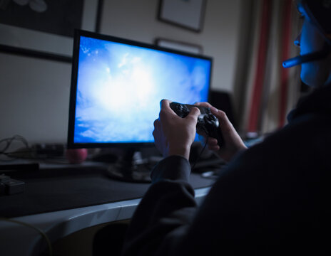 Teenage Boy Playing Video Game At Computer In Dark Bedroom