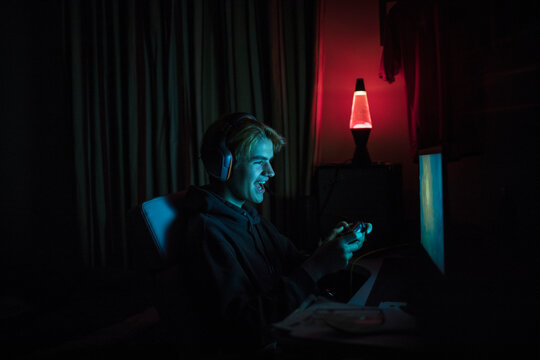 Smiling teenage boy playing video game at computer in dark bedroom
