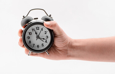 Hand holding a black alarm clock on white background