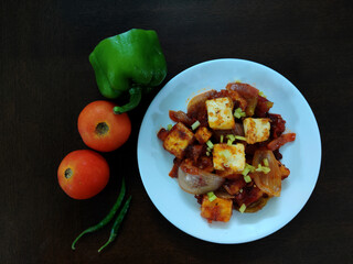 Served plate of Indian Crispy Chilli Paneer along with fresh vegetables in a white plate on a wooden table
