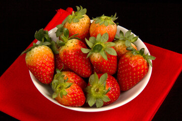 Red fresh strawberry in a bowl on black background.