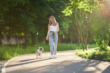 Smiling woman walking with french bulldog in park. © serhiibobyk