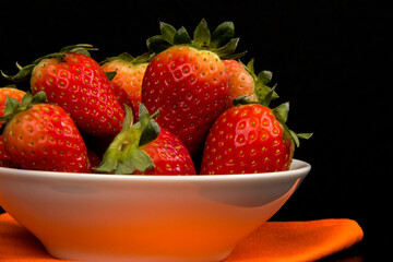 Red fresh strawberry in a bowl on black background.