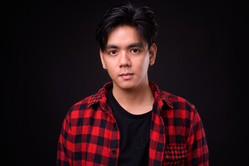 Young handsome Asian hipster man against black background