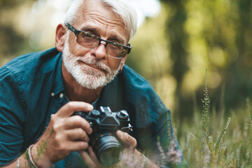 Elderly man takes pictures of flowers in park, pensioner on walk. Active hobby of mature person.