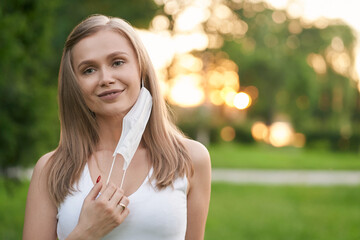 Smiling woman taking off white face mask.