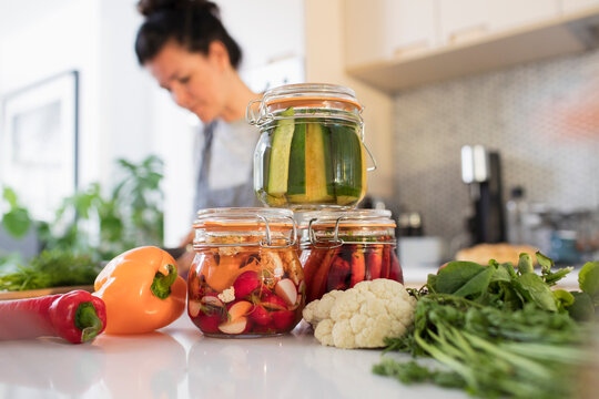 Woman preserving vegetables in jars at kitchen counter