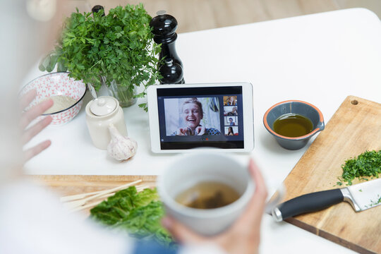 Woman drinking tea and cooking while video chatting with friends - Powered by Adobe