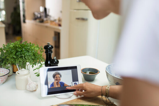 Woman video chatting with friends on digital tablet screen in kitchen