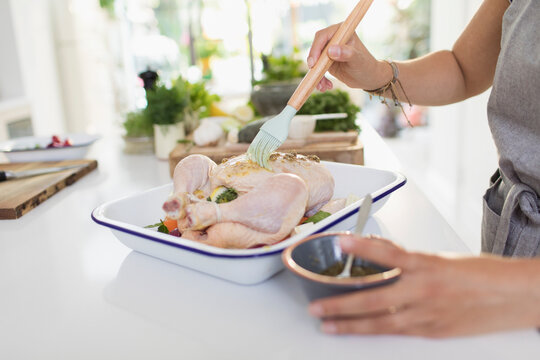 Woman brushing raw chicken with sauce in kitchen