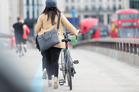 Businesswoman walking bicycle along city bridge, London, UK