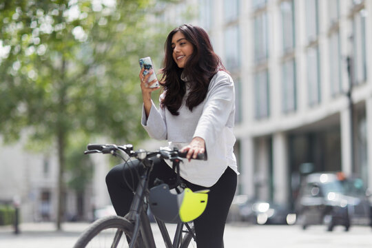 Woman on bicycle using smart phone on sunny city street