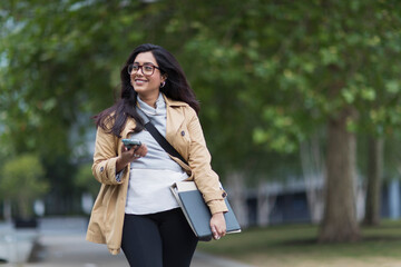 Smiling businesswoman walking with smart phone in park