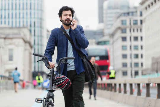 Businessman with bicycle talking on smart phone on city bridge