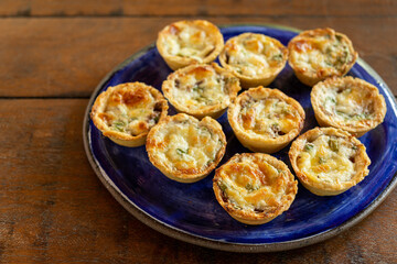 Brazilian gastronomy. Cheese and dried meat pies with arugula in handmade dish on wooden table.