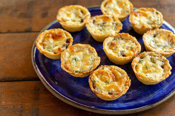 Brazilian gastronomy. Cheese and dried meat pies with arugula in handmade dish on wooden table.