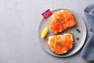 Sandwich, toast with smoked salmon and cream cheese on plate with Norwegian flag. Grey background. Top view.