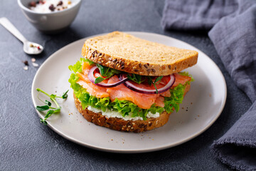 Sandwich with salmon, vegetables and cream cheese on plate. Grey background. Close up.