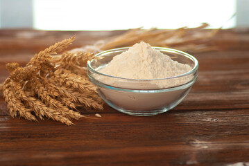 Glass bowl with flour and branches of natural wheat on the dark brown wooden table