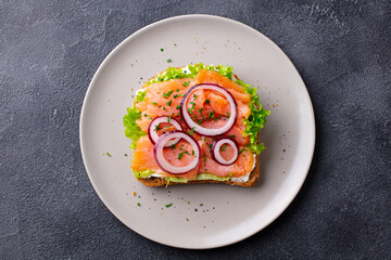 Sandwich with salmon, vegetables and cream cheese on plate. Dark background. Top view.