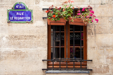 Fototapeta na wymiar A window with shutters, bars and flower boxes is set into a stone wall on a street in Paris, France.