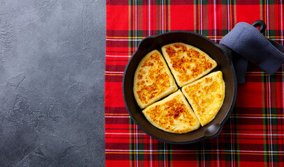 Traditional Scottish tattie potato scones in cast iron pan. Plaid fabric napkin background. Copy space. Top view.