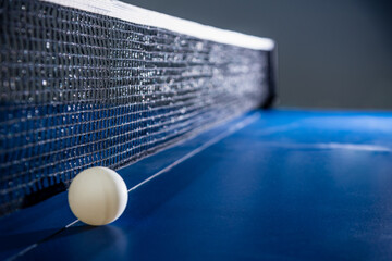 Closeup one white ball on the blue ping pong table with a black net, Table tennis paddle is a sports competition equipment indoor activity and exercise for concept background