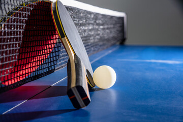 Closeup black and red table tennis racket a white ball on the blue ping pong table with a net, Table tennis paddle is a sports competition equipment indoor activity and exercise for concept background