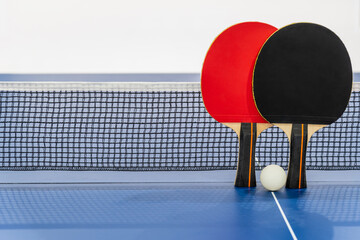 Black and red table tennis racket and a white ball on the blue ping pong table with a net, Two...