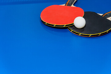 Black and red table tennis racket and a white ping pong ball on the blue ping pong table, Two table tennis paddle is a sports competition equipment for indoor exercise