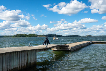 One woman sits with her back on the wooden pier and looks into the distance. Summer beautiful...