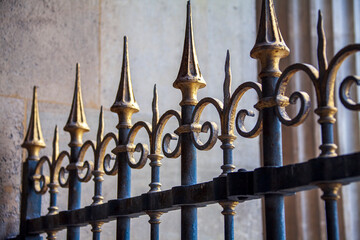 A palace gate with wrought iron posts painted blue and gold leaf points on top surrounds a palace...