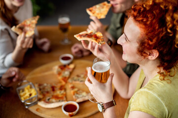 Happy woman drinking beer and eating pizza with friends in a pub.
