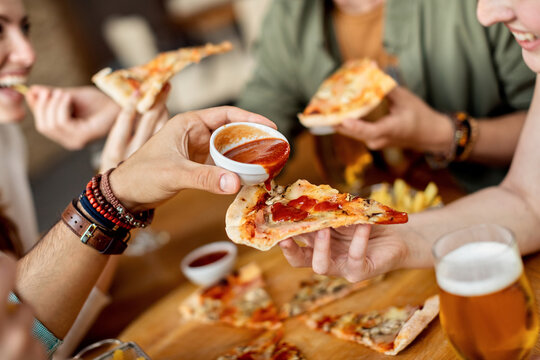 Close-up of friends adding ketchup on pizza while eating in a pub.